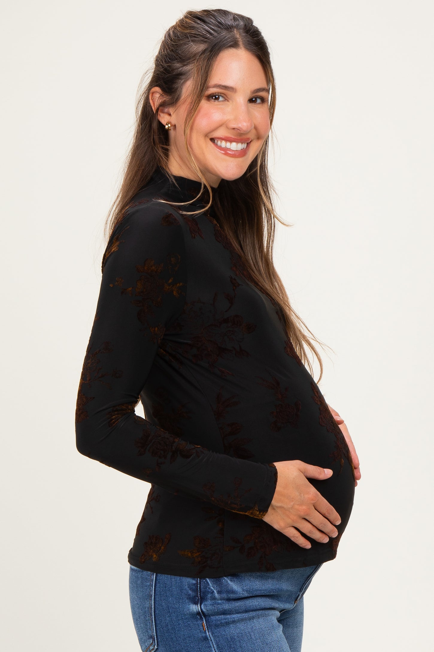 woman wearing a black long sleeve maternity top with floral details, smiling and showing her baby bump