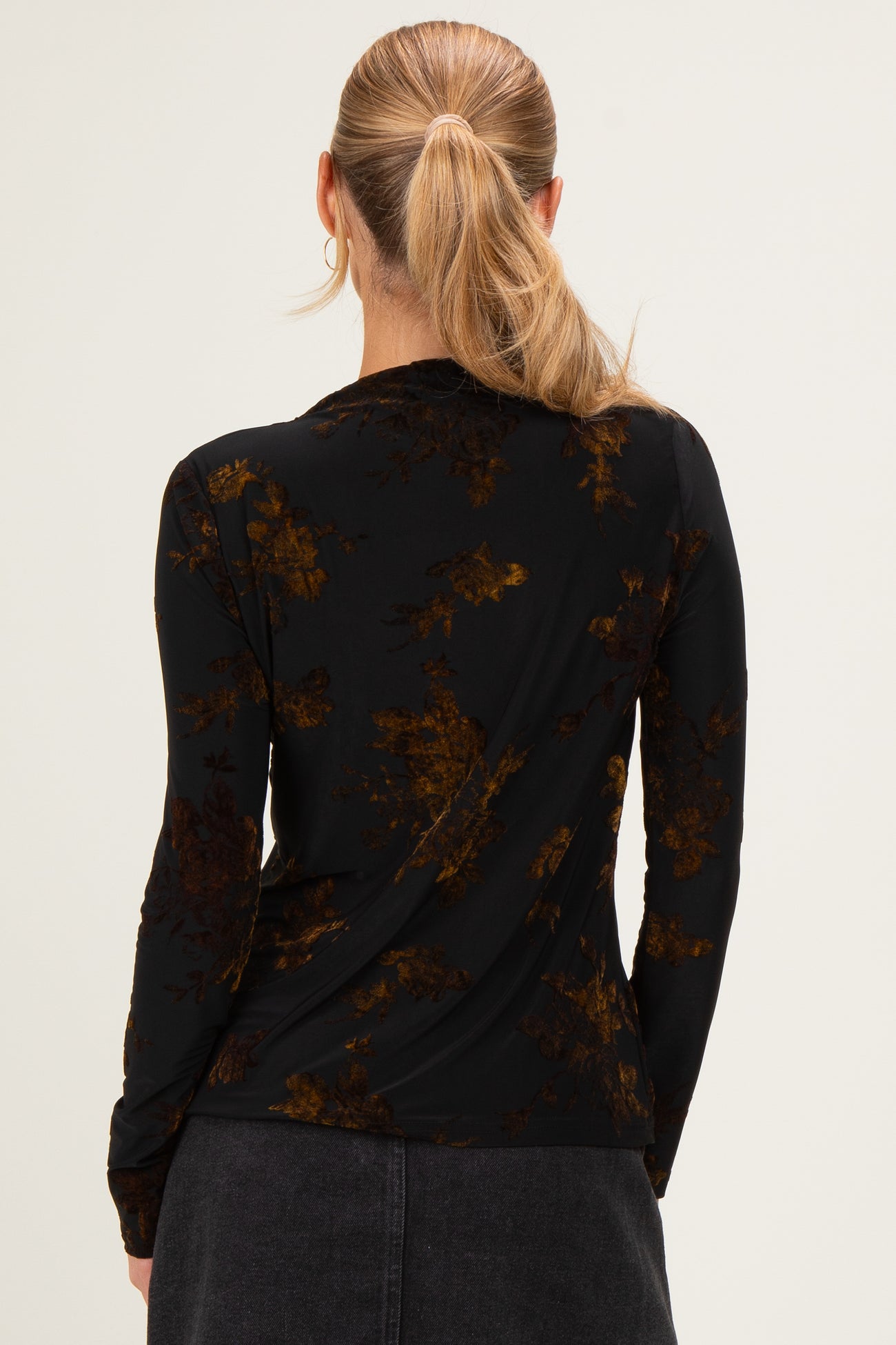 woman wearing a black long sleeve top with a floral print in shades of brown and gold, seen from the back