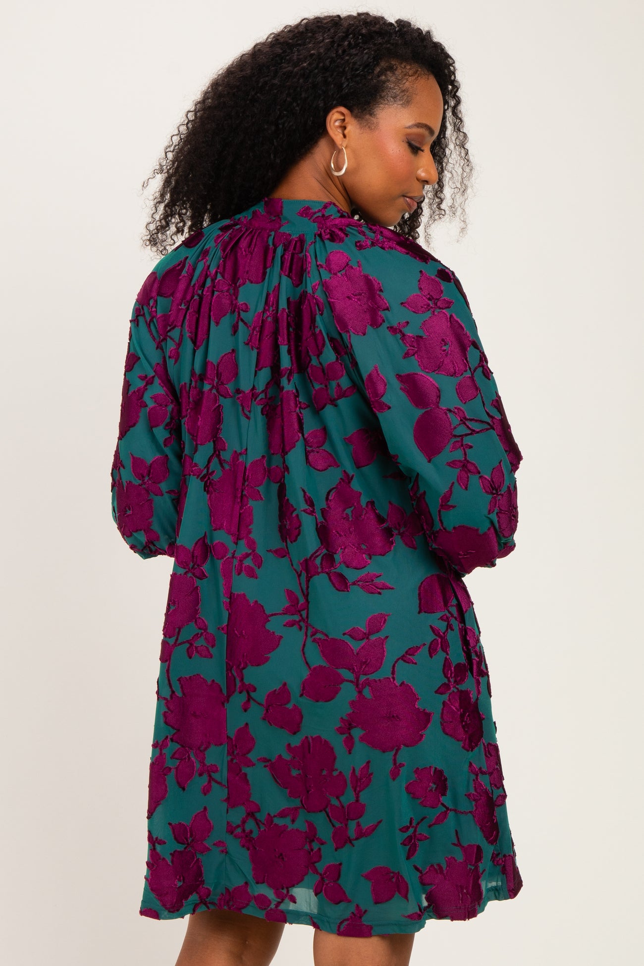 woman wearing a teal dress with a maroon floral print and gathered detailing at the back