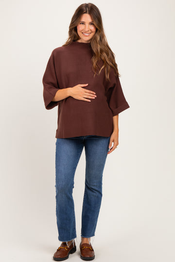 woman wearing a brown maternity top with three-quarter sleeves and holding her baby bump, paired with blue skinny jeans