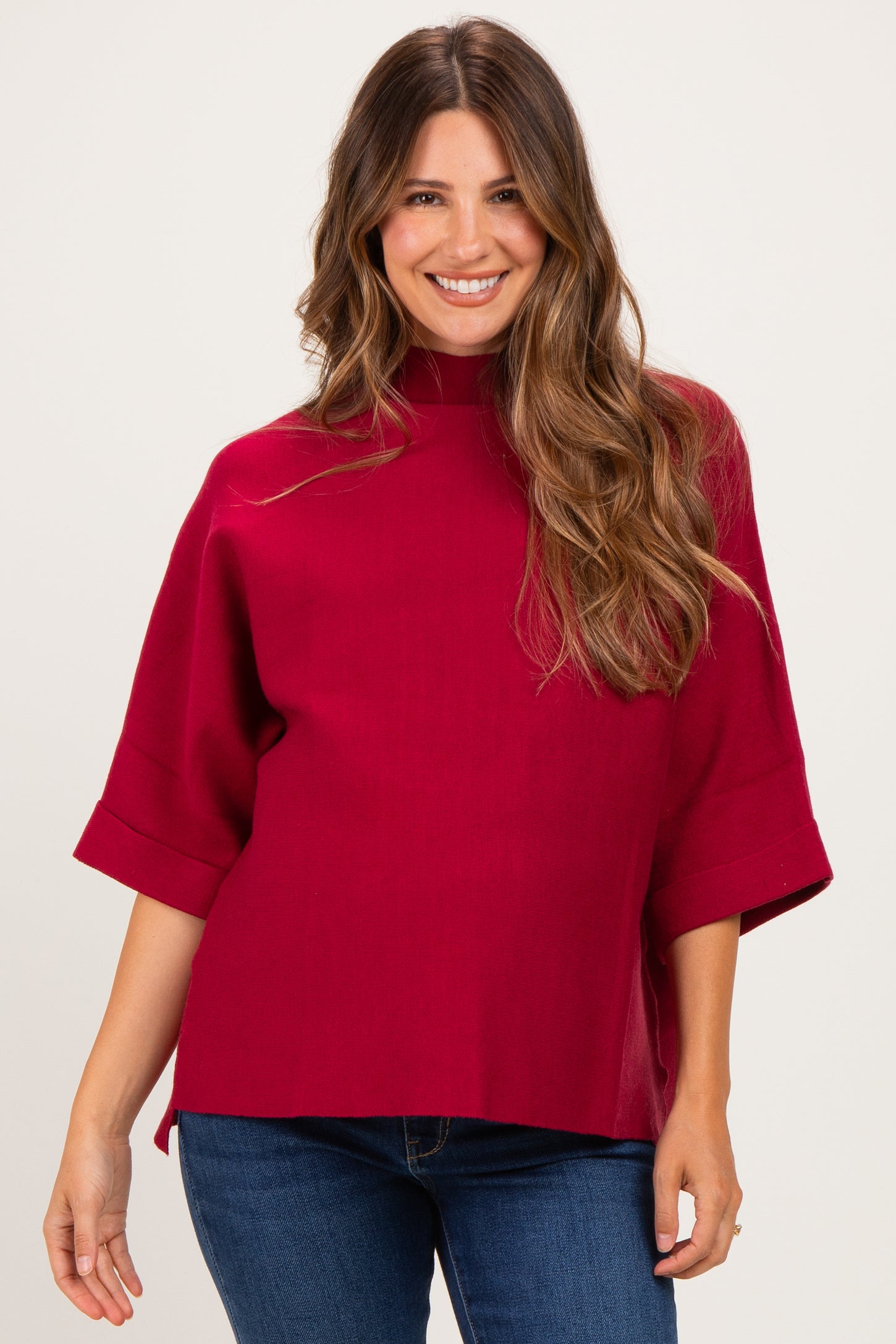 woman wearing a burgundy maternity top with a high neck and short sleeves, smiling at the camera