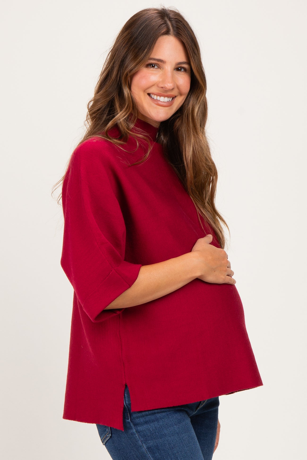 woman wearing a burgundy maternity top with short sleeves and side slits, cradling her baby bump
