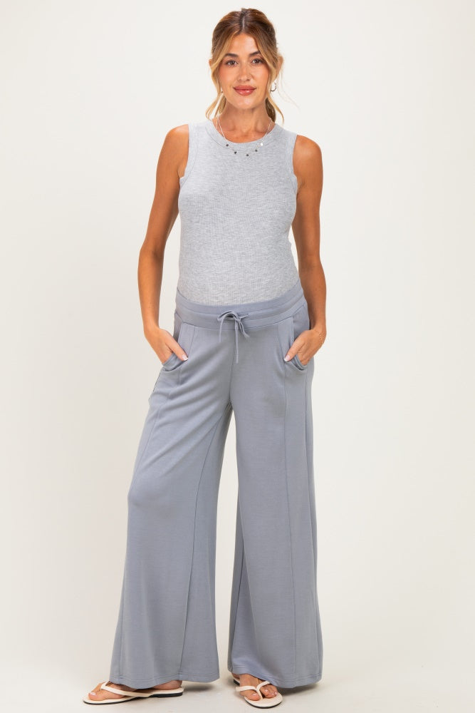 woman wearing a light gray sleeveless maternity top and wide-leg maternity pants with pockets, showing her baby bump