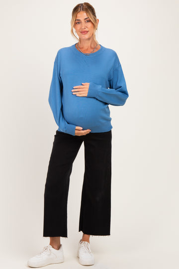 woman wearing a blue maternity sweater and black wide-leg pants, holding her baby bump
