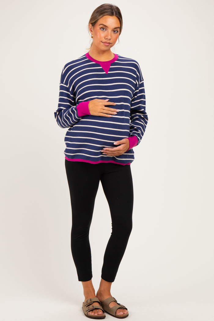 woman wearing a navy and white striped maternity sweatshirt with pink accents and holding her baby bump, paired with black leggings