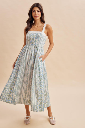 woman wearing a floral printed maxi dress with a fitted bodice, square neckline, and pockets, posed against a neutral background