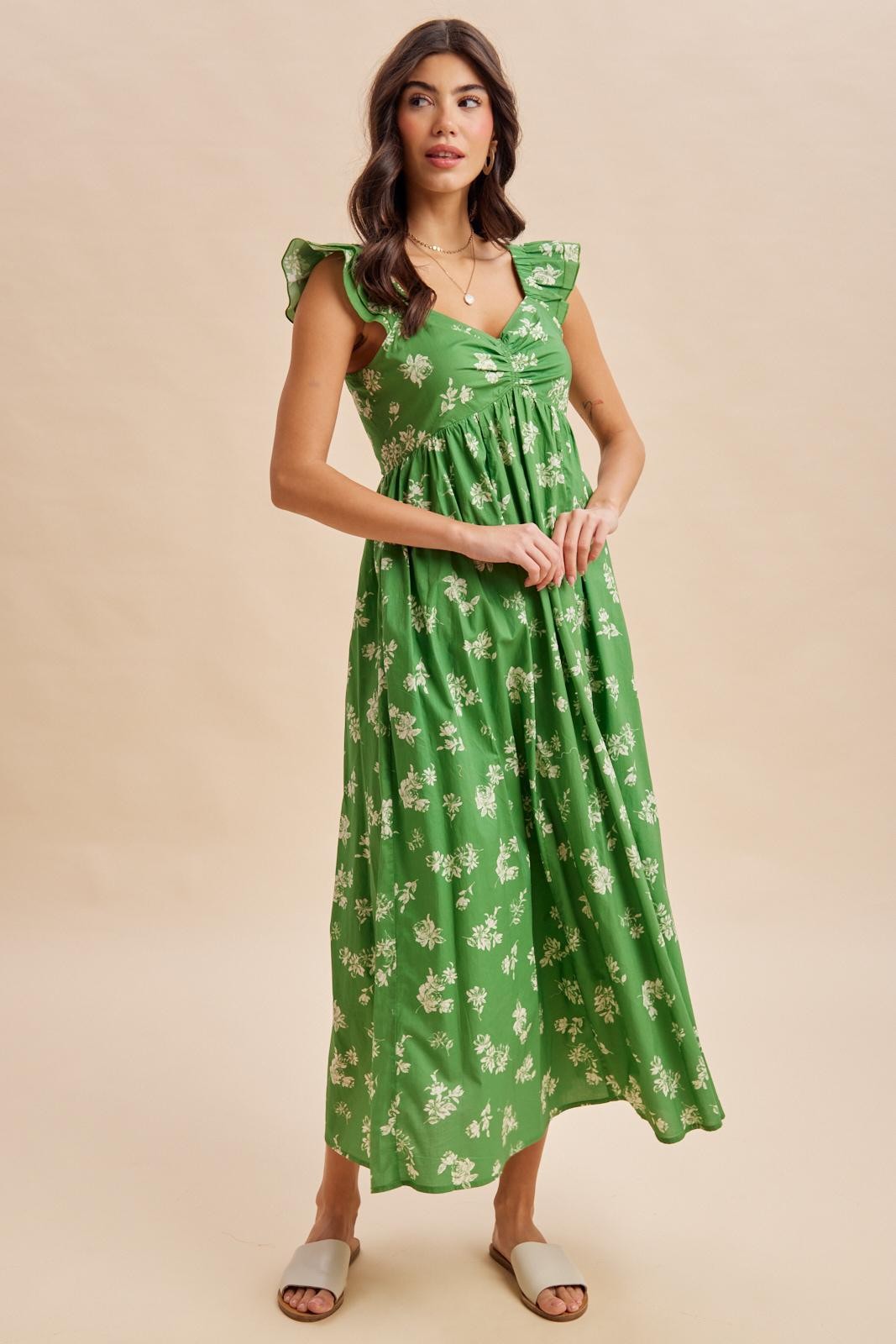 woman wearing a green floral maxi dress with ruffled sleeves and a cinched waist, standing against a neutral background
