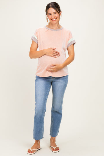 woman wearing a striped short sleeve maternity top and blue jeans, gently cradling her baby bump