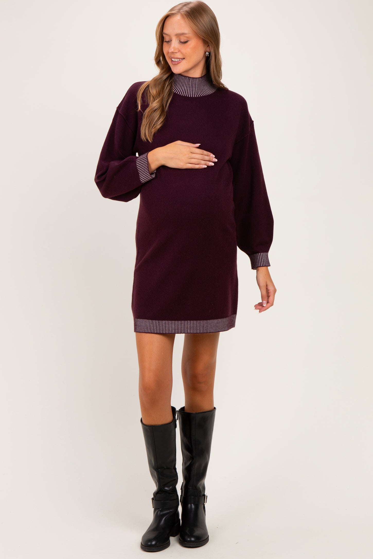 woman wearing a burgundy maternity sweater dress with striped collar and sleeves, holding her baby bump
