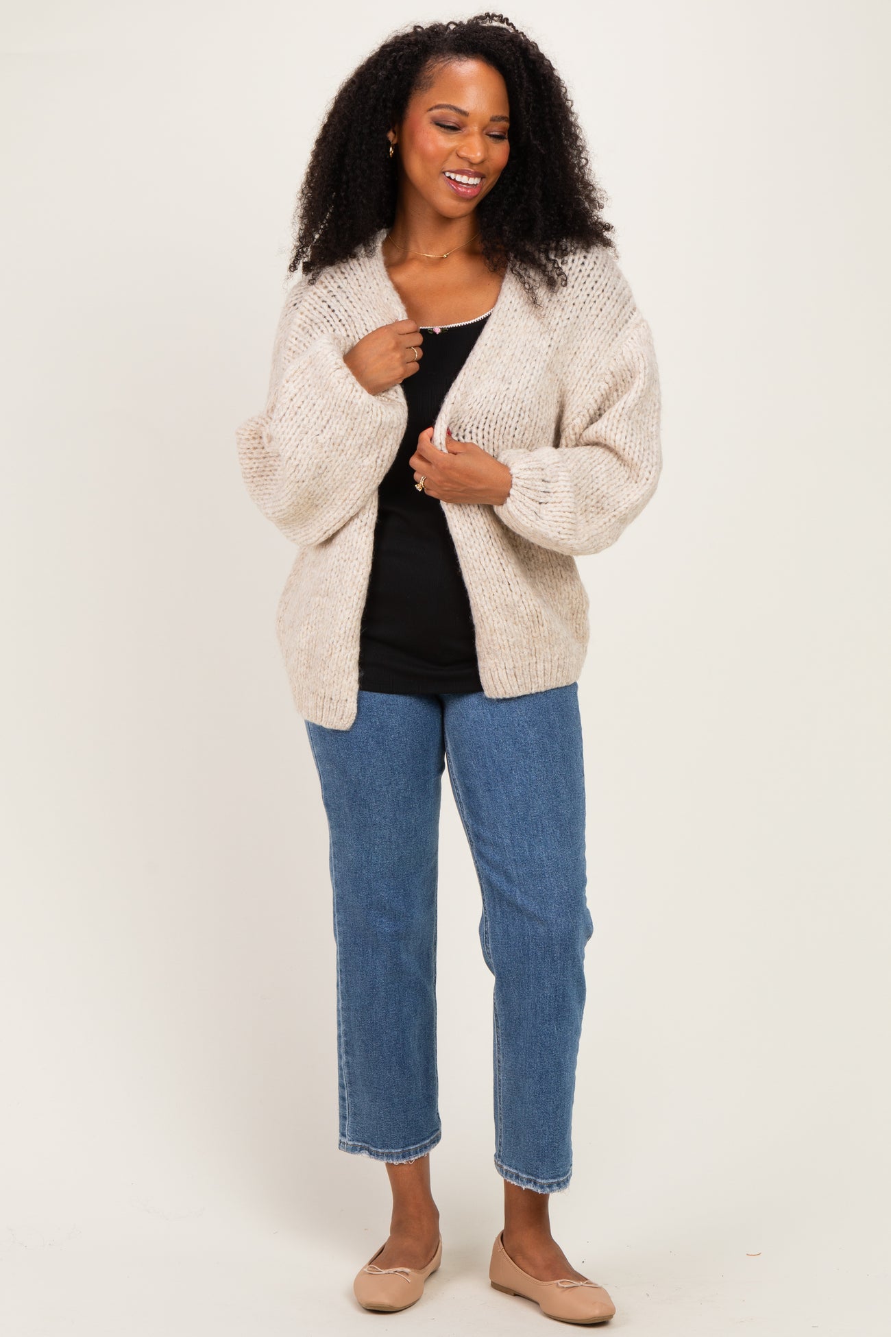 woman wearing a cream chunky knit cardigan over a black tank top and blue straight-leg jeans with beige flats