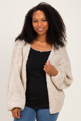 woman wearing a chunky beige knit cardigan over a black tank top and blue jeans, smiling at the camera