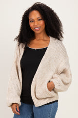 woman wearing a cozy beige oversized knitted cardigan over a black top with jeans and smiling at the camera