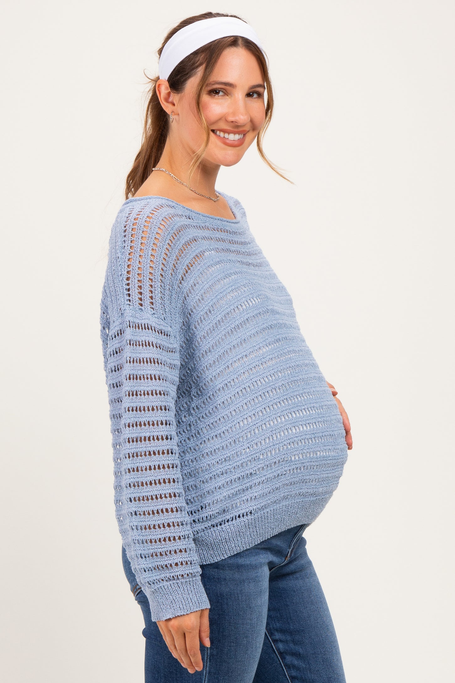 woman wearing a light blue maternity sweater with a relaxed fit and open knit pattern, showing her baby bump