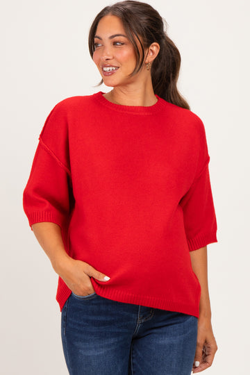 woman wearing a red oversized maternity sweater with short sleeves and a relaxed fit, smiling and touching her belly