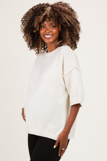 woman wearing a cream oversized maternity sweater with short sleeves and a visible baby bump