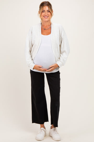 woman wearing a light gray maternity zip-up jacket over a white tank top and black wide-leg pants, showing her baby bump