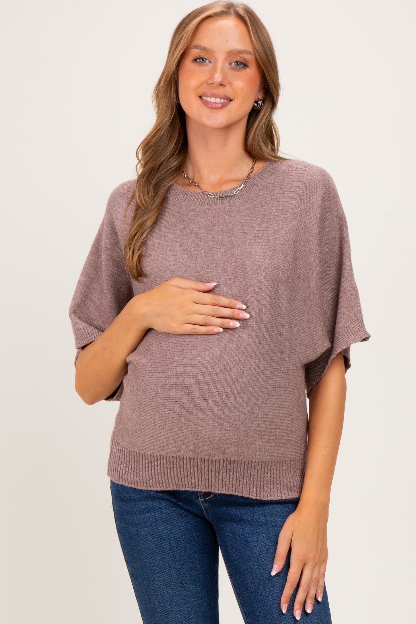 woman wearing a mauve short sleeve maternity sweater and holding her baby bump