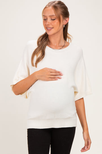 woman wearing a cream short sleeve maternity sweater and cradling her baby bump