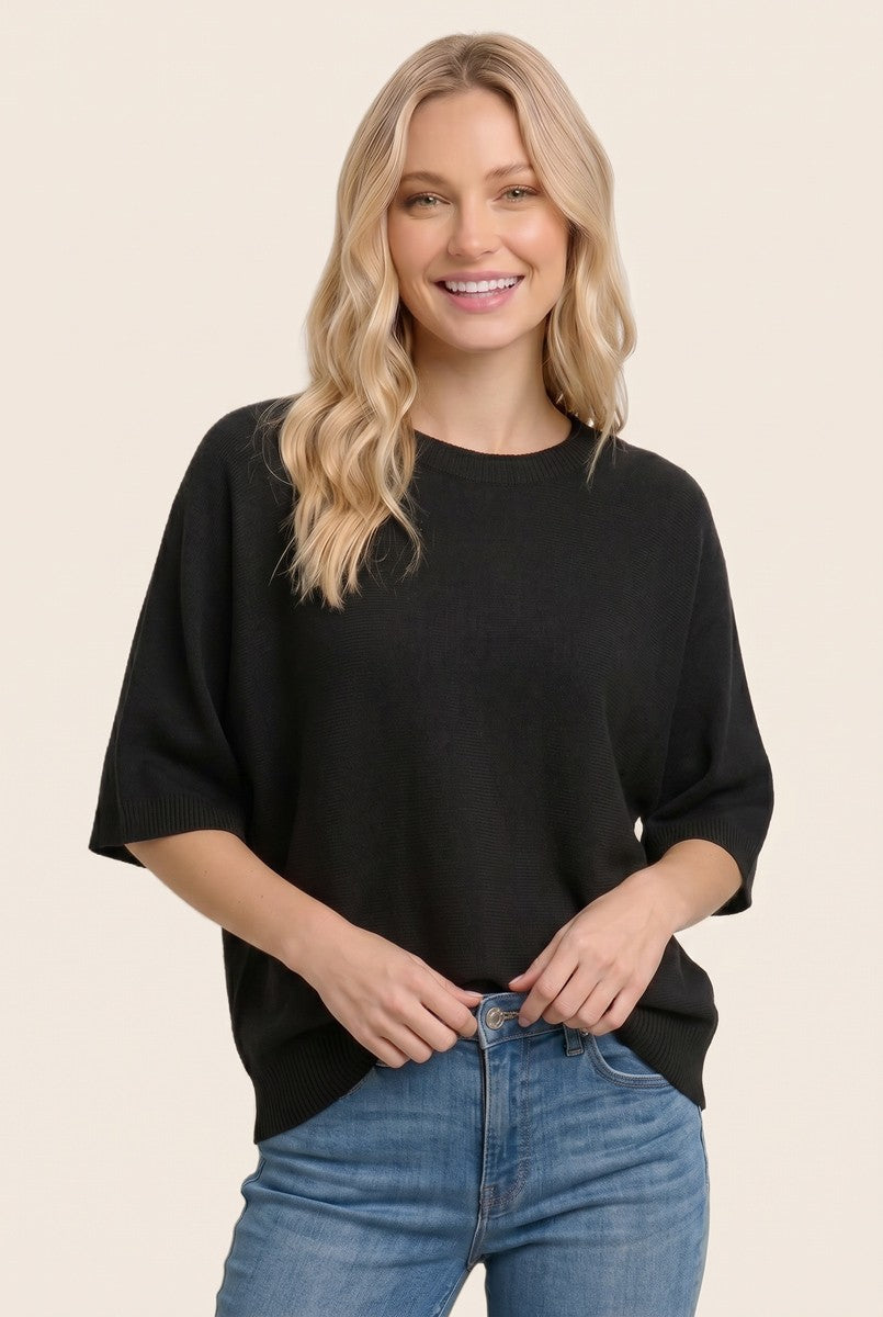 woman wearing a black oversized short sleeve sweater with a round neckline and relaxed fit paired with light blue jeans
