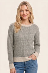 woman wearing a gray striped sweater with a cream hem and cuffs, smiling against a light background