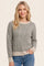 woman wearing a gray striped sweater with a cream hem and cuffs, smiling against a light background
