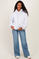 woman wearing a light gray maternity hoodie with a relaxed fit and blue flared jeans, holding her baby bump