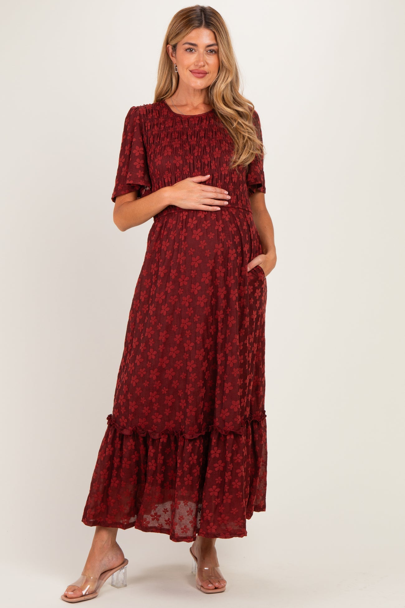 woman wearing a burgundy floral maternity dress with a ruffled hem and short sleeves, holding her baby bump