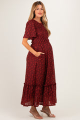 woman wearing a burgundy floral print maxi maternity dress with short sleeves and pockets, showcasing her baby bump