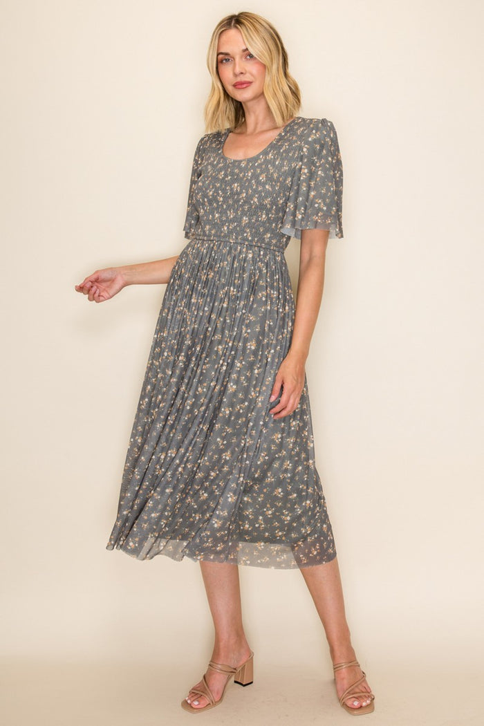 woman wearing a grey floral midi dress with short flutter sleeves and a flowing skirt