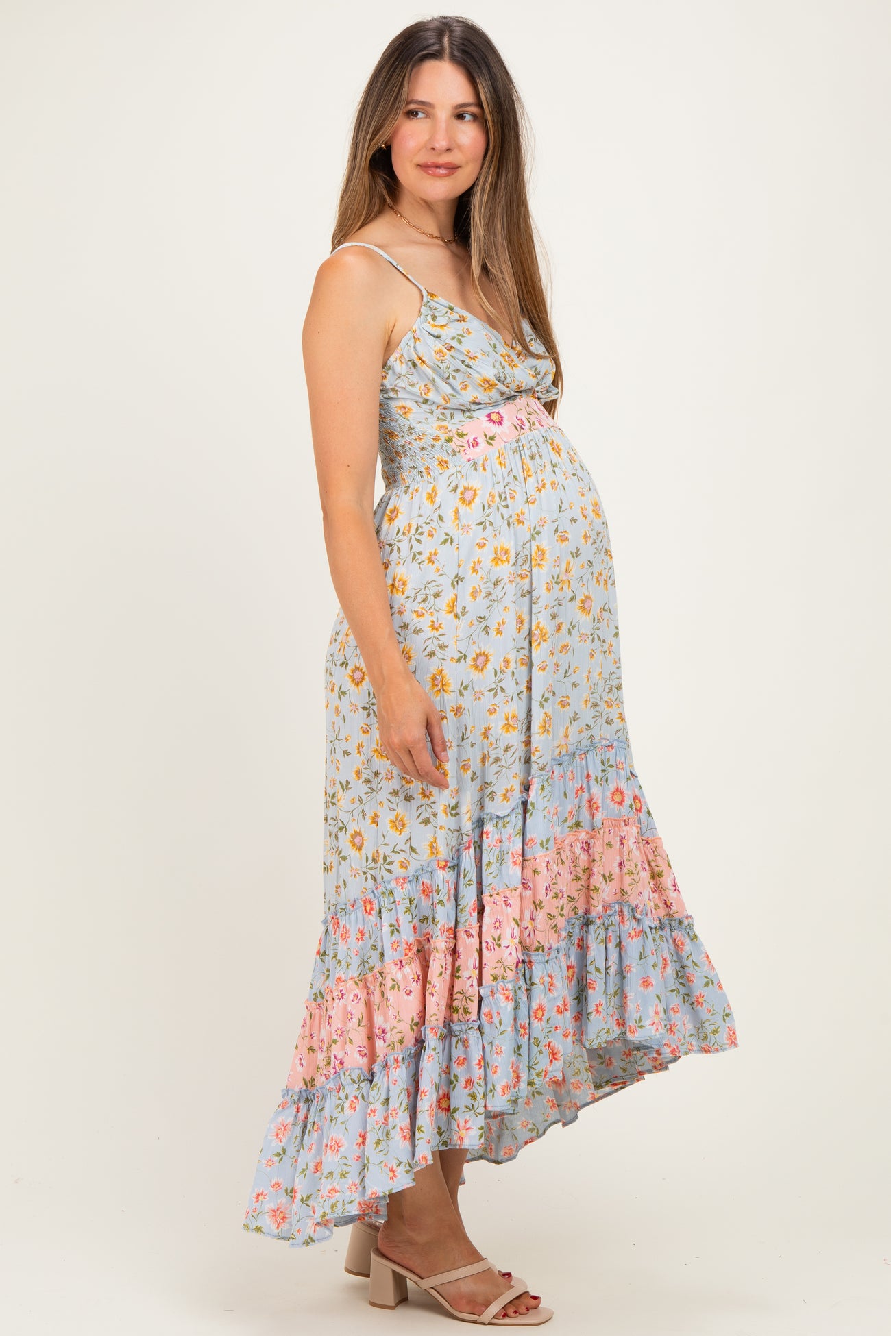 woman wearing a light blue floral maternity dress with adjustable straps and a ruffled hem, showcasing her baby bump