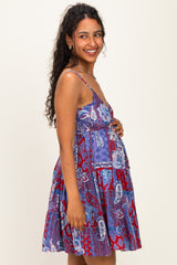 woman wearing a purple and red paisley print maternity dress, smiling and showing her baby bump