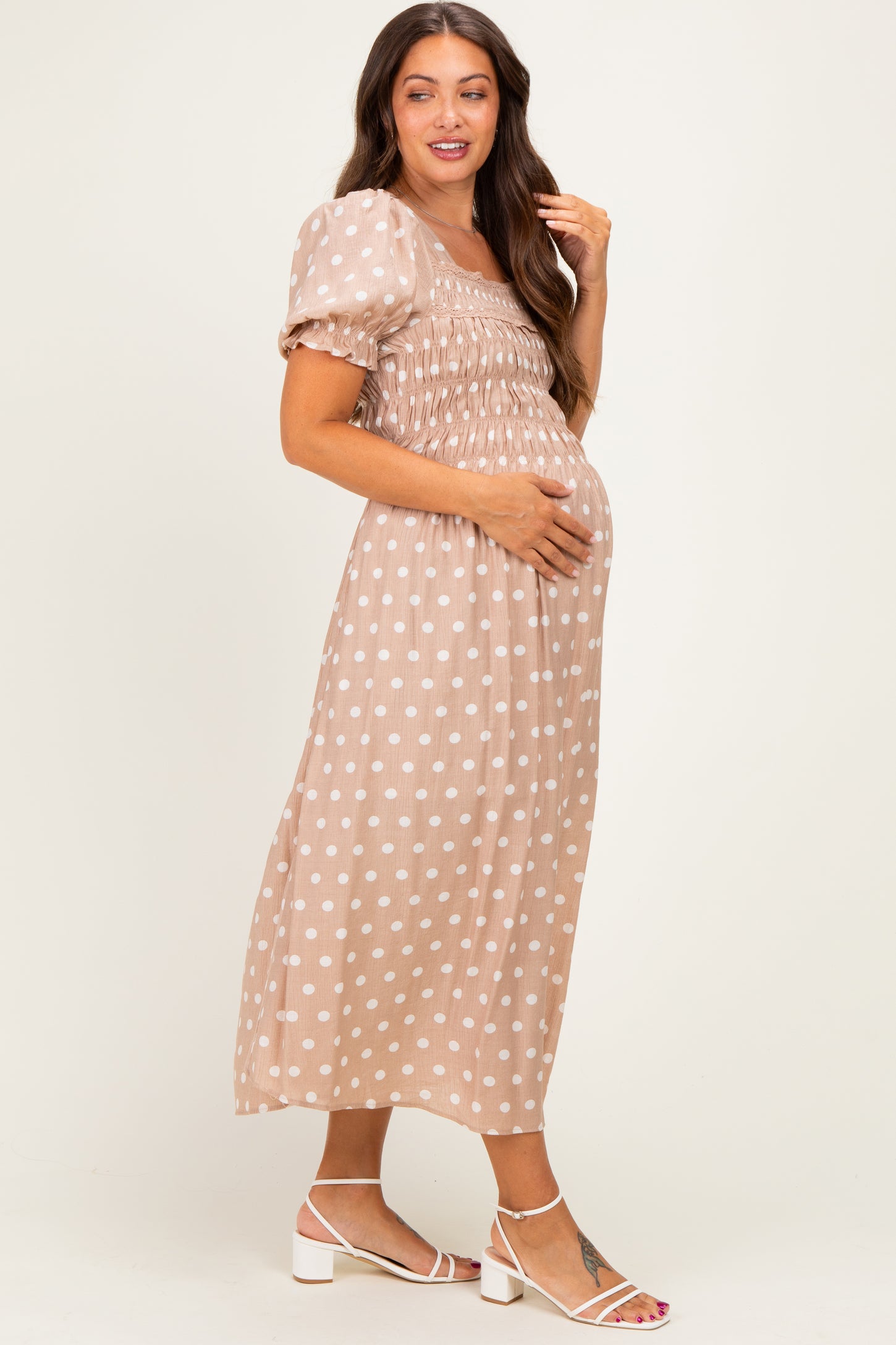 woman wearing a beige polka dot maternity dress with puff sleeves and smocked bodice, showing her baby bump