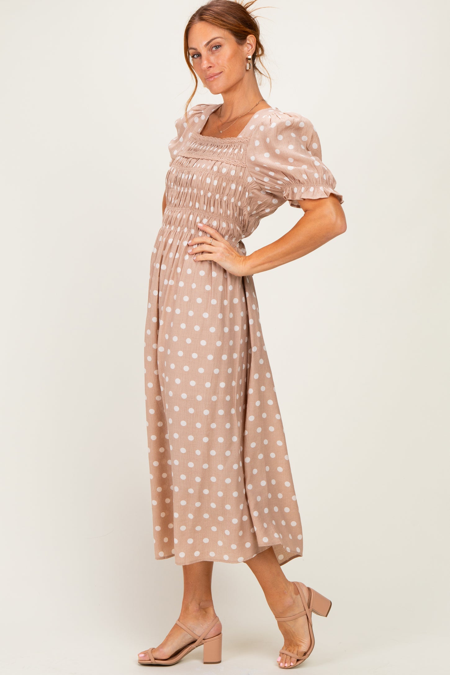 woman wearing a taupe polka dot midi dress with puff sleeves and smocked bodice, posed against a neutral background
