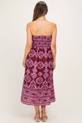 woman wearing a strapless burgundy maternity dress with white fabric pattern, showing her back and flowing mid-calf length