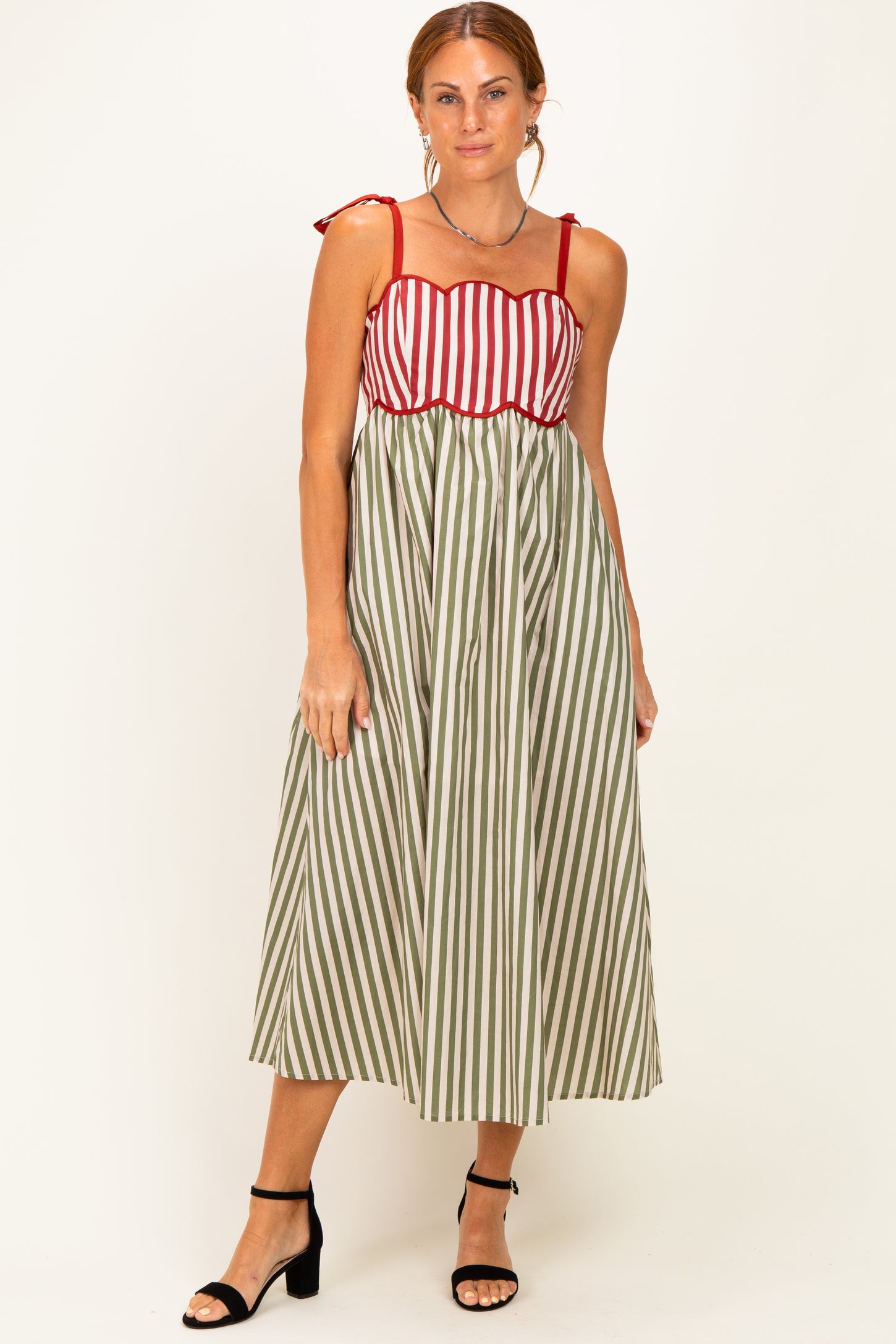 woman wearing a midi dress with red and white striped top and green and white striped skirt, styled with black heels