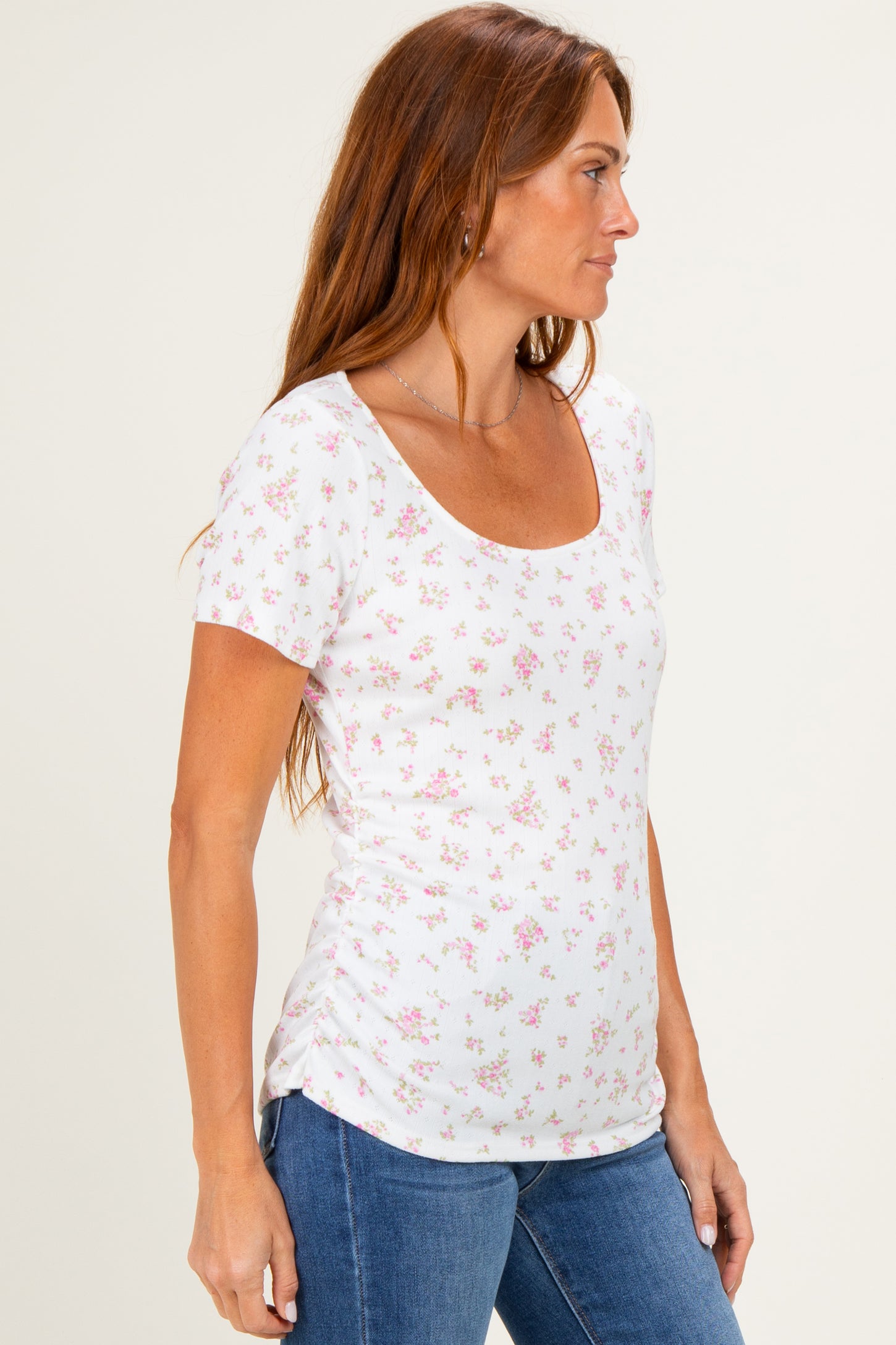 woman wearing a white short sleeve top with a pink floral print and side ruching, paired with blue jeans