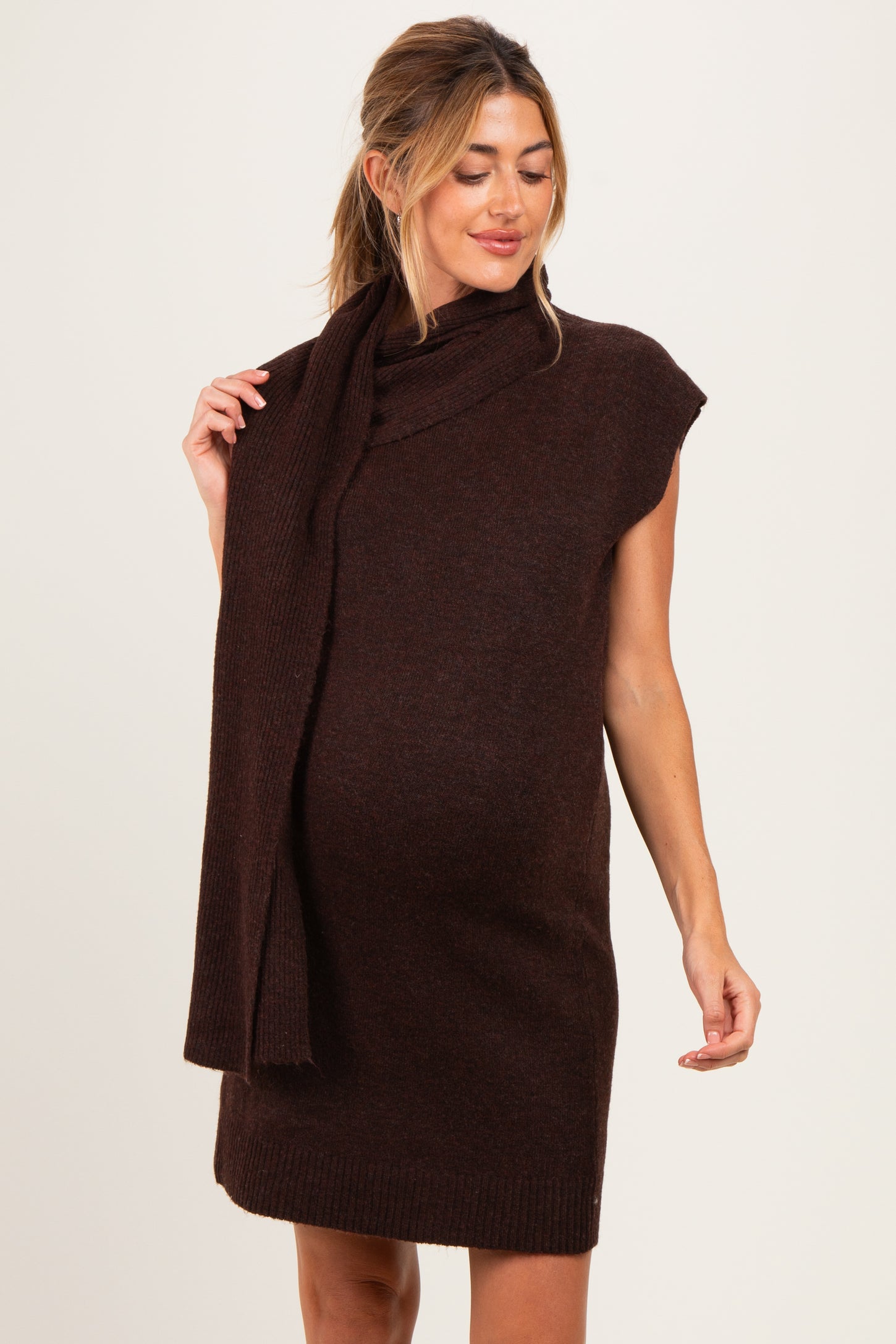woman wearing a brown sleeveless maternity sweater dress with a matching scarf and showcasing her baby bump
