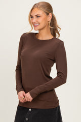 woman wearing a brown long sleeve top with a round neckline and fitted silhouette, smiling against a neutral background