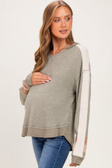 woman wearing a green maternity sweater with color-blocked sleeves and holding her baby bump