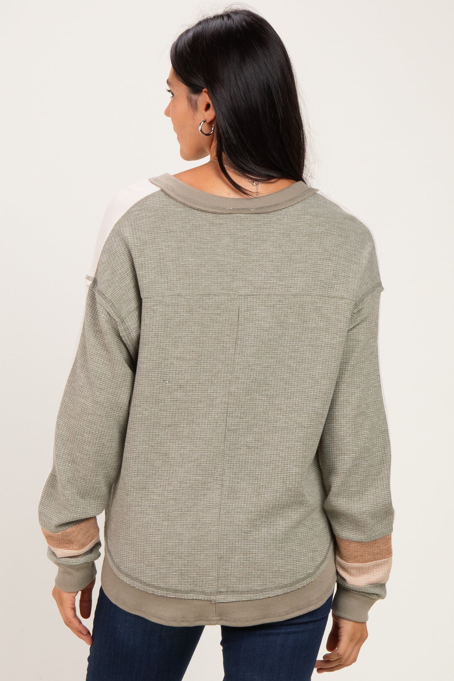 woman wearing a light green oversized sweater with color block sleeves and a relaxed fit, viewed from the back
