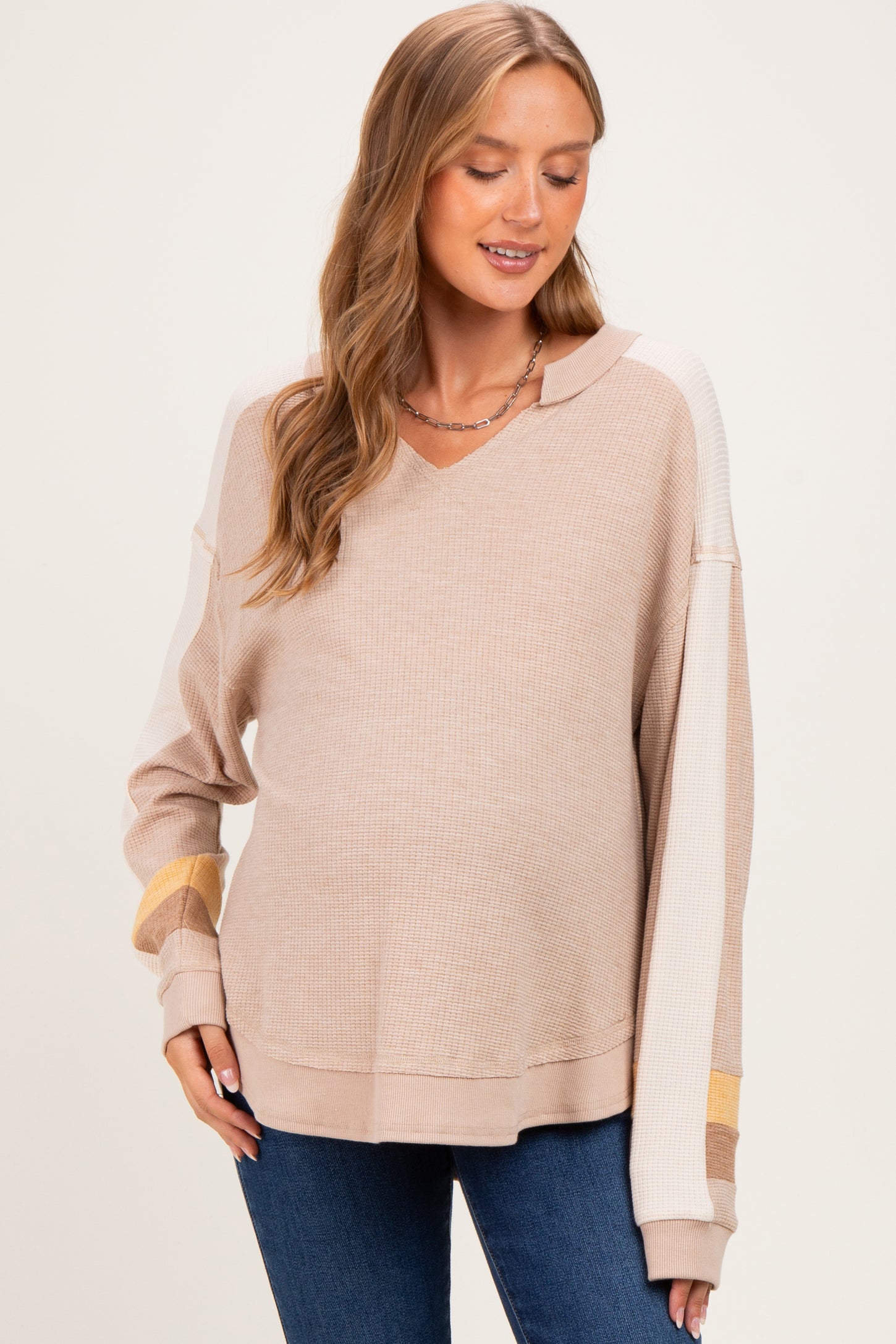 woman wearing a beige maternity wear v-neck sweater with taupe and mustard stripes and a visible baby bump