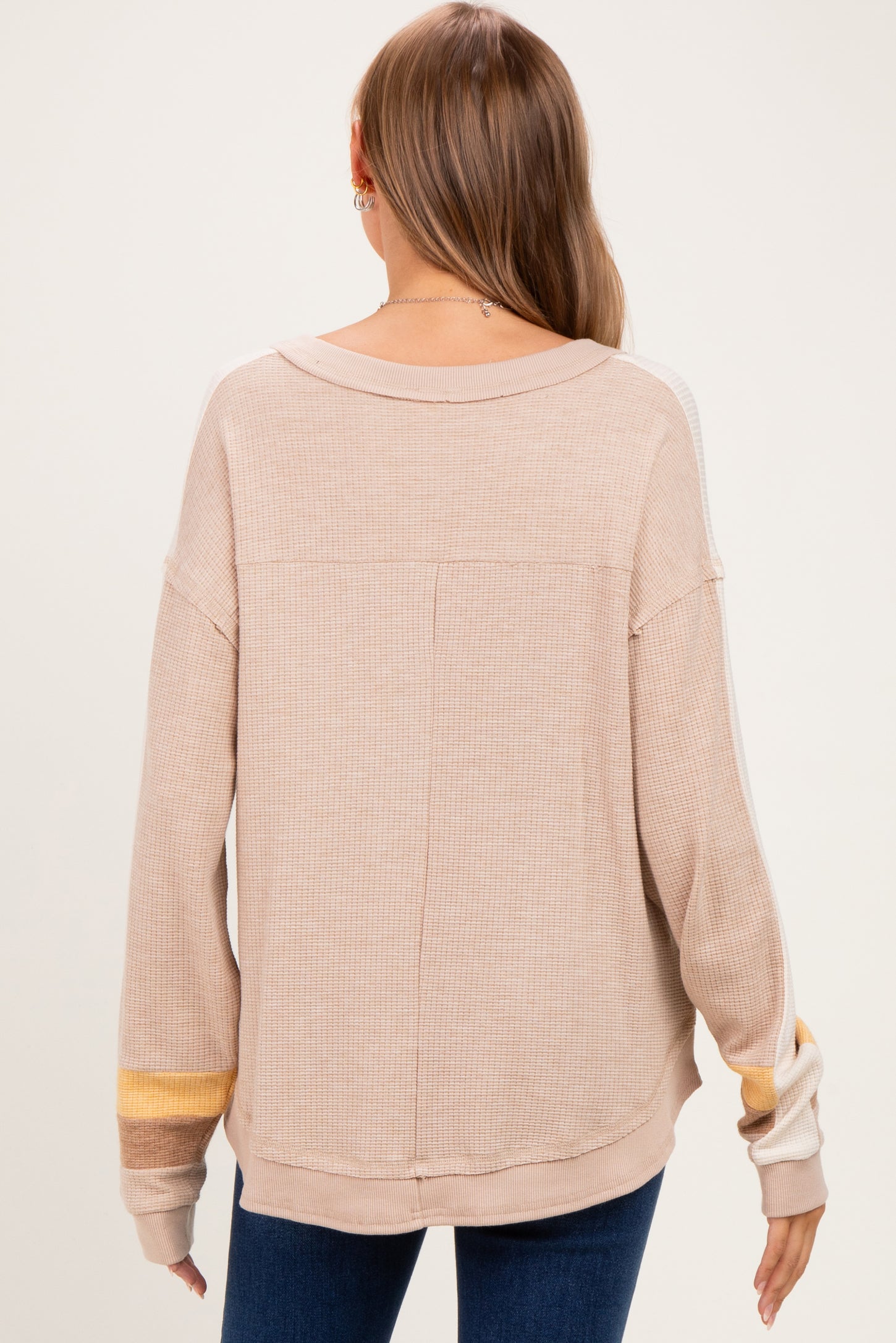 woman wearing a beige maternity top with a relaxed fit and color-blocked sleeves, seen from the back