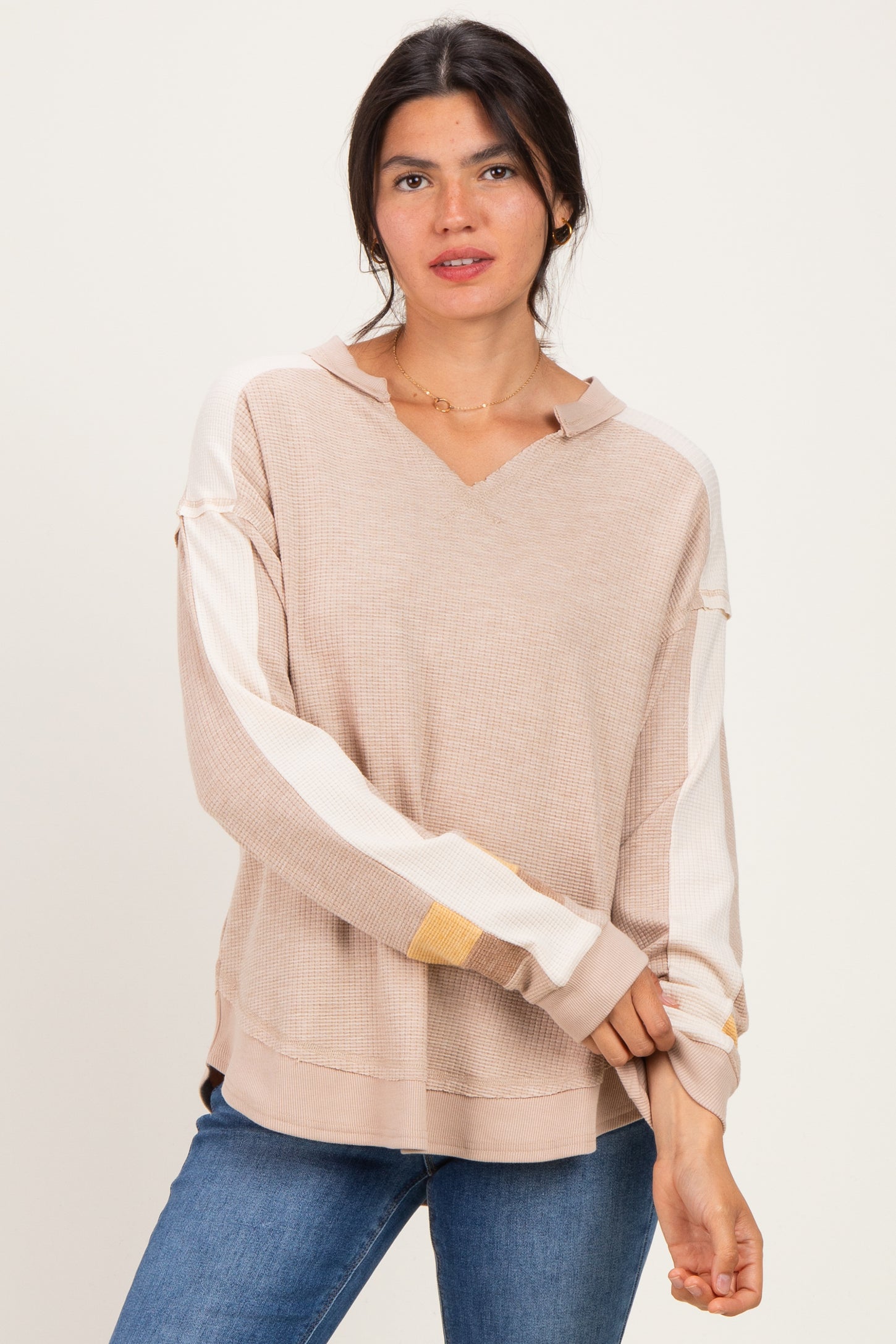 woman wearing a beige v-neck hoodie with contrasting striped sleeves and a relaxed fit paired with blue jeans