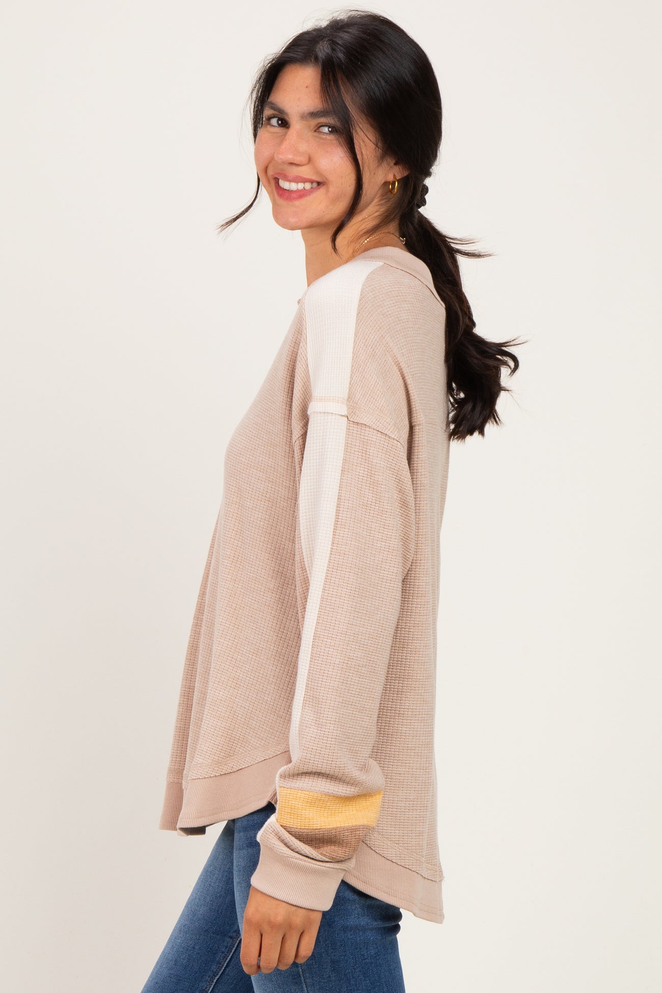 woman wearing a beige long sleeve sweater with color block sleeves and smiling at the camera