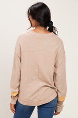 woman wearing a tan oversized long sleeve top with yellow stripe detail on the sleeves, standing backwards