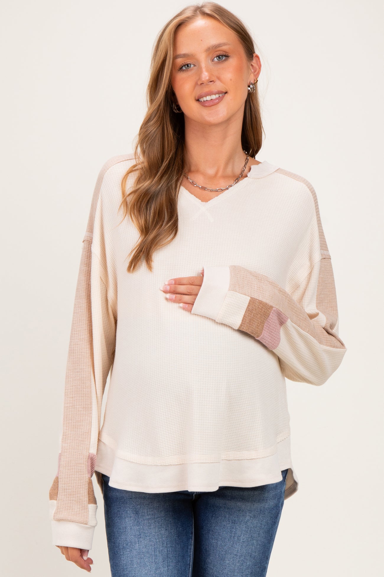 woman wearing a neutral colored maternity long sleeve top with color block sleeves and a visible baby bump