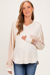 woman wearing a neutral colored maternity long sleeve top with color block sleeves and a visible baby bump