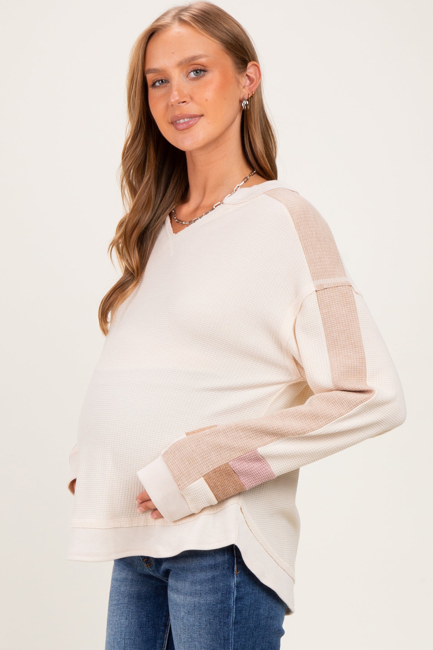 woman wearing a cream-colored maternity top with color-blocked sleeves and a visible baby bump