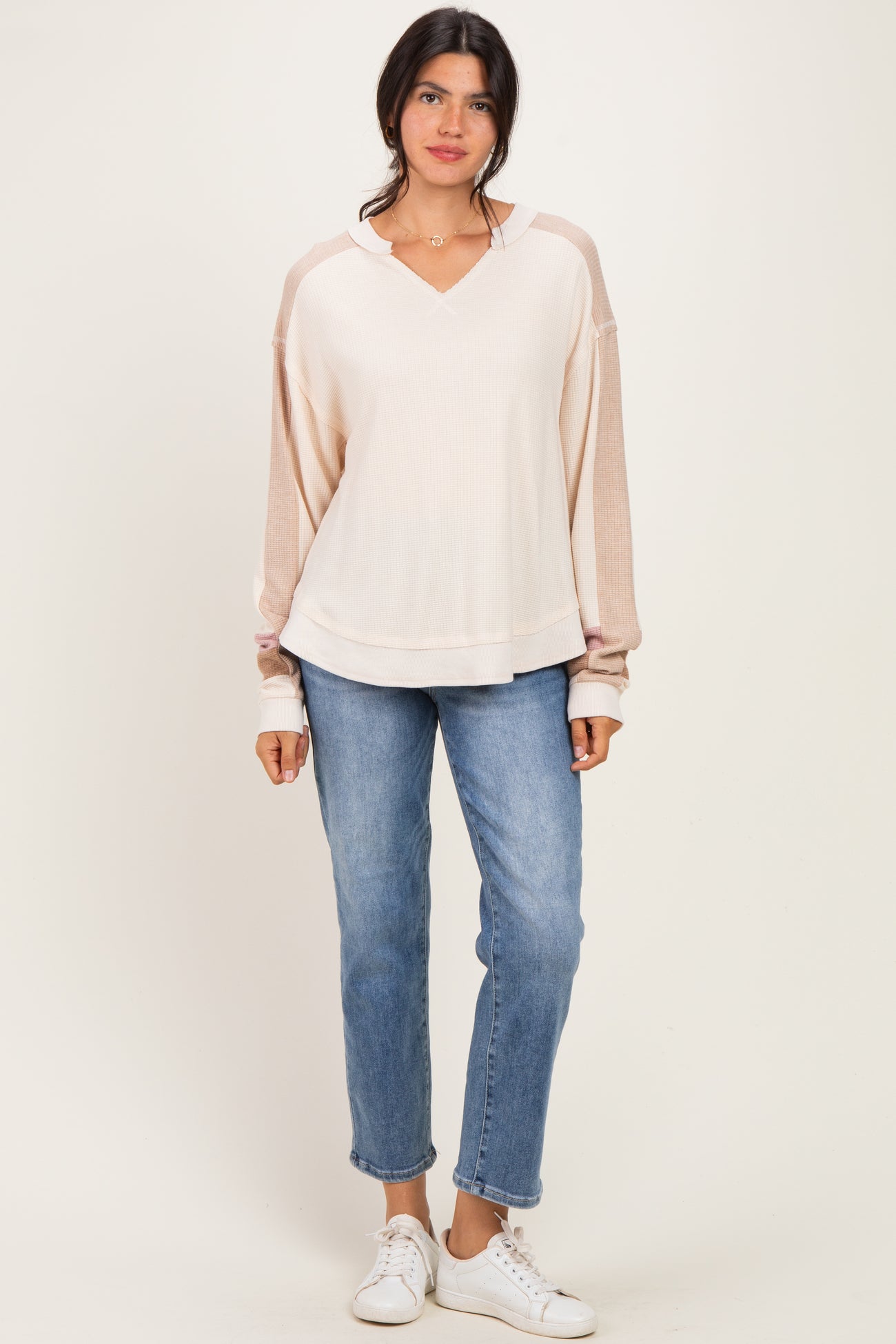 woman wearing a light pink long sleeve hoodie paired with blue jeans and white sneakers