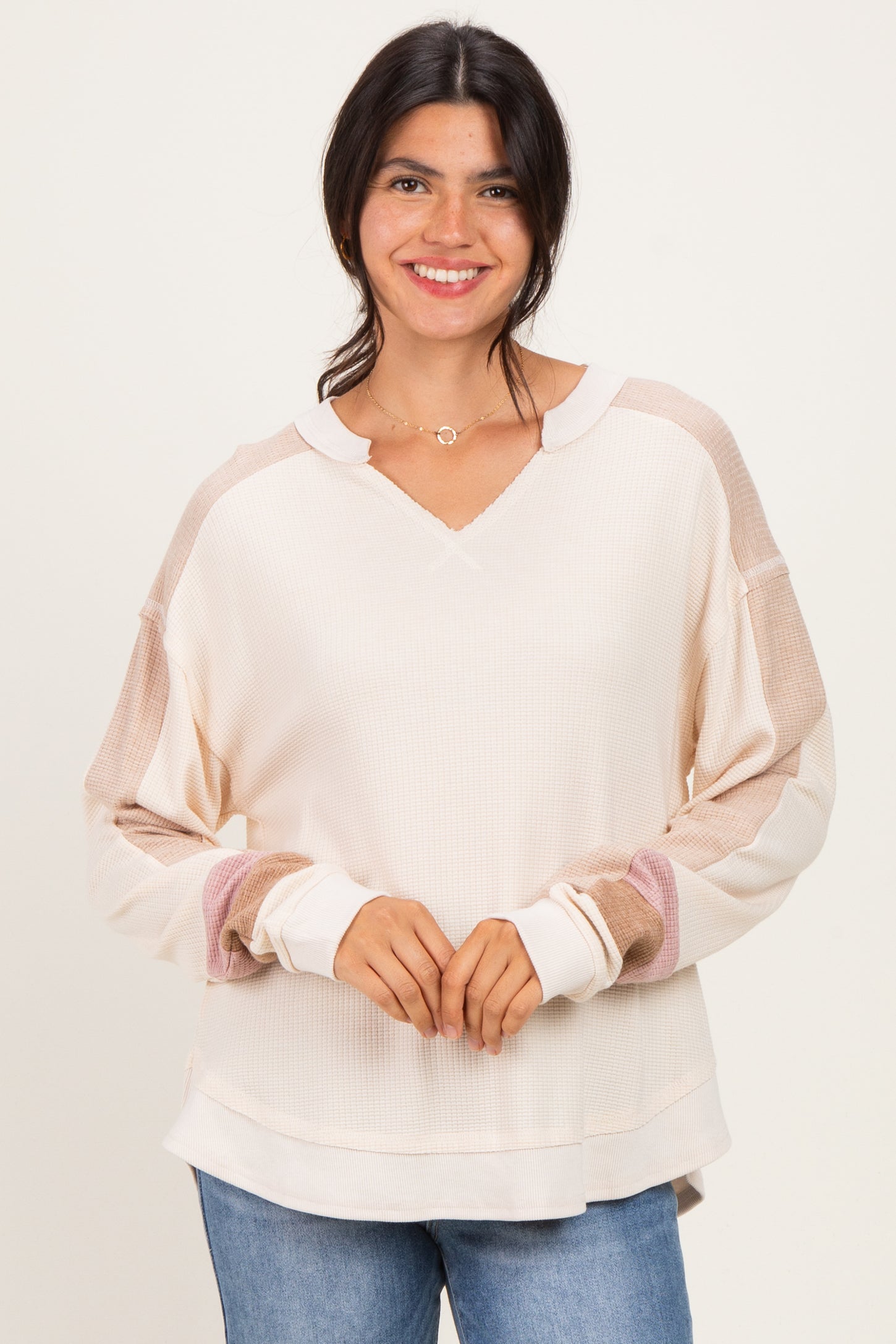 woman wearing a cream-colored long sleeve top with color-blocked sleeves and a v-neckline, smiling at the camera